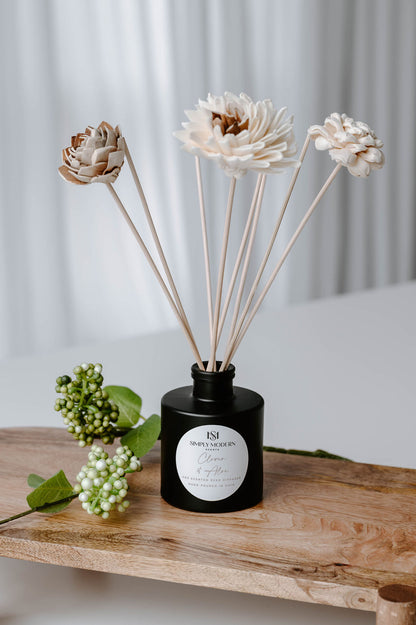 Clover & Aloe handmade floral reed diffuser on a wood riser with green berry sprigs