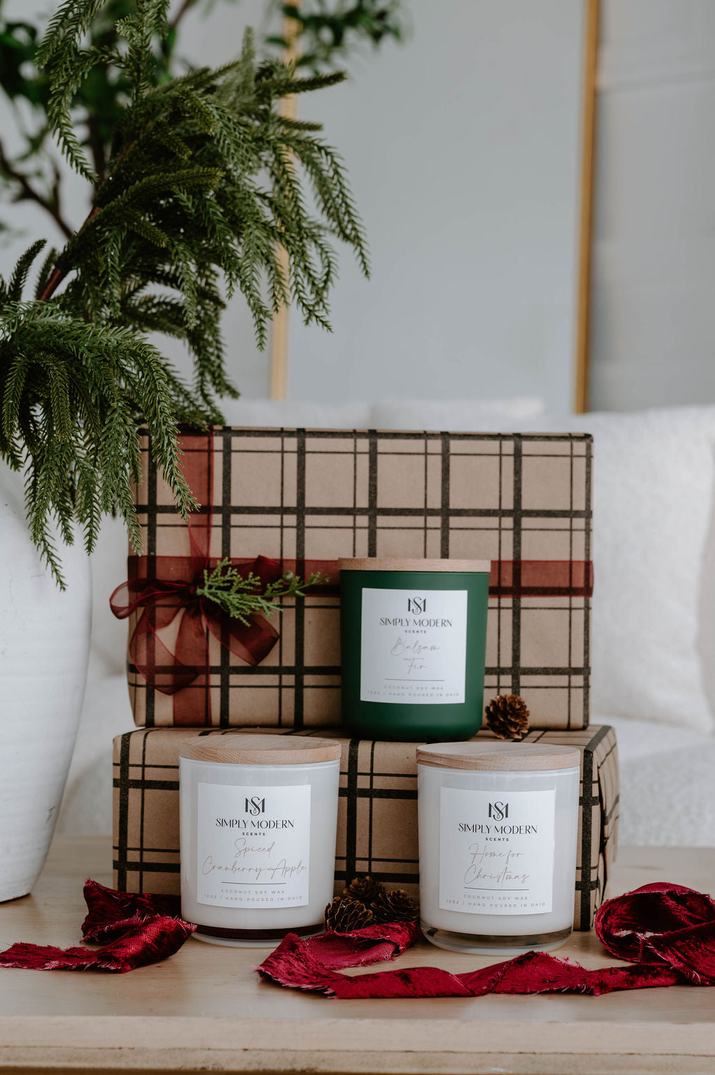 Holiday candle gift set of three 12 oz wood-wick candles beside a white vase of winter greenery