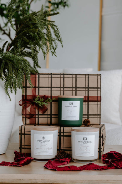 Holiday candle gift set of three 12 oz wood-wick candles beside a white vase of winter greenery