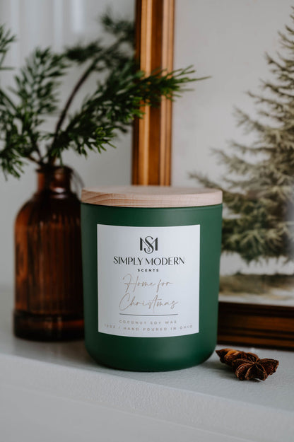 Home for Christmas 12 oz wood-wick coconut soy candle in an olive green vessel with a wooden lid, styled on a white mantel with pine and star anise