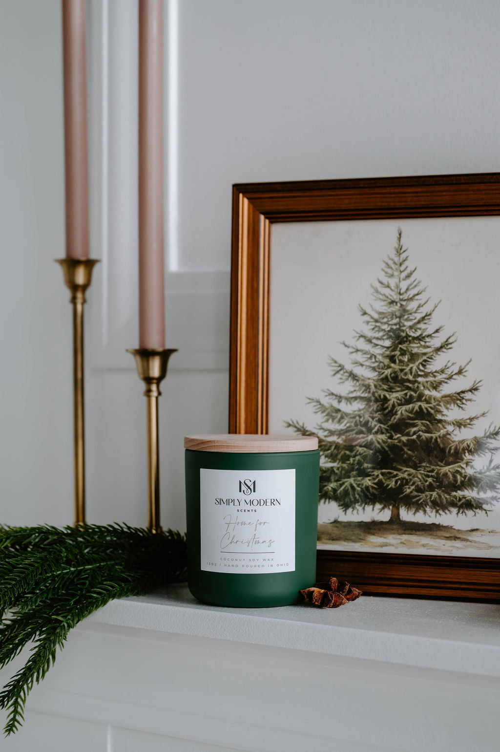Home for Christmas olive green candle on a mantel with brass candlesticks and a framed pine print
