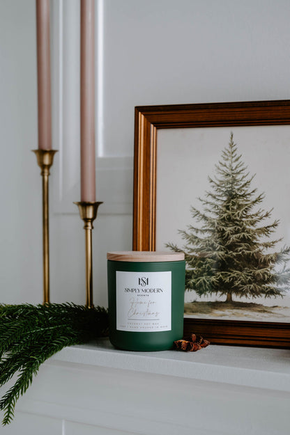 Home for Christmas olive green candle on a mantel with brass candlesticks and a framed pine print
