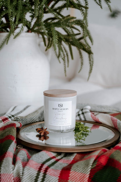 Home for Christmas 12 oz wood-wick coconut soy candle in a white vessel with a wooden lid on a mirrored tray with holiday plaid