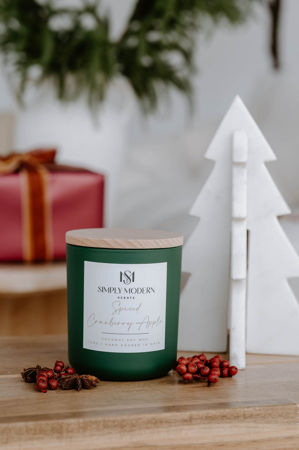Spiced Cranberry Apple 12 oz wood-wick coconut soy candle in an olive green vessel with a wooden lid, styled with red berries and a marble tree