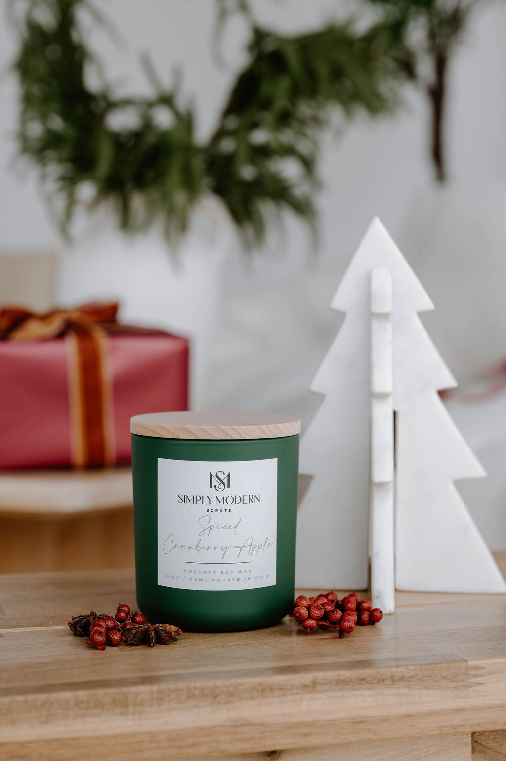 Spiced Cranberry Apple olive green candle on a wood table with winter berries and a wrapped gift