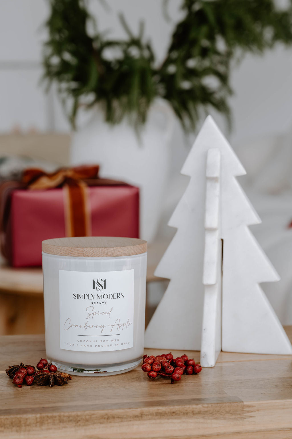 Spiced Cranberry Apple white candle on a wood table with winter berries and a wrapped gift