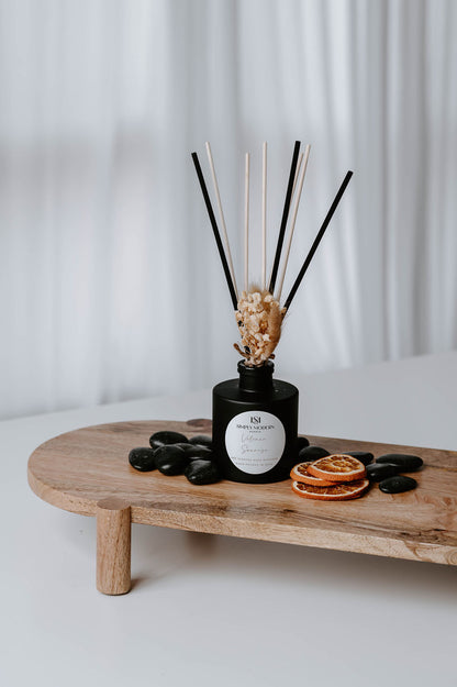 Volcano Sunrise reed diffuser on a wood riser with black river stones and dried citrus