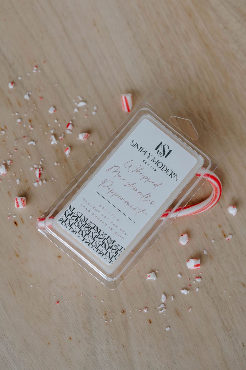 Whipped Marshmallow Peppermint 4 oz coconut soy wax melt clamshell on a wood table with a candy cane and crushed peppermint