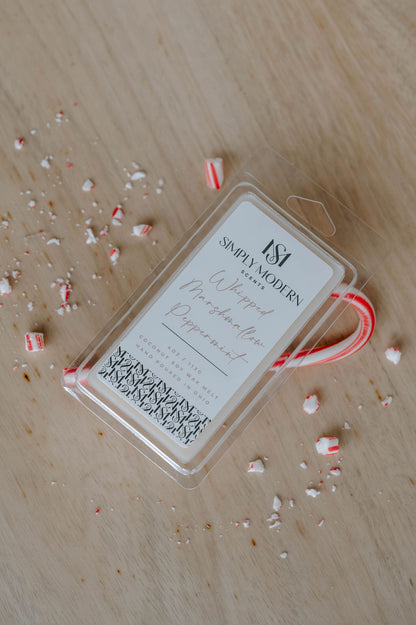 Whipped Marshmallow Peppermint 4 oz coconut soy wax melt clamshell on a wood table with a candy cane and crushed peppermint
